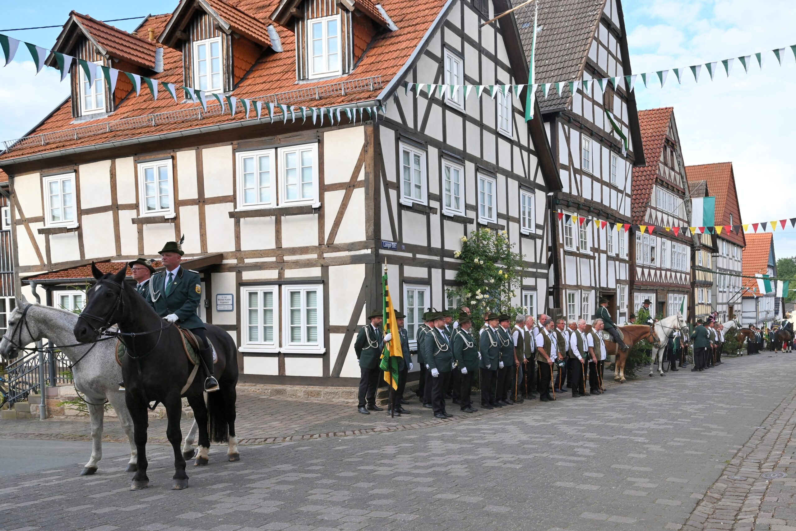 Altstädter Männerkompanie beim Antreten in der Lange Straße in Mengeringhausen zum Freischießen 2024. Im Vordergrund stehen Hauptmann und Adjutant zu Pferd, dahinter die angetretene Kompanie mit Fahne.